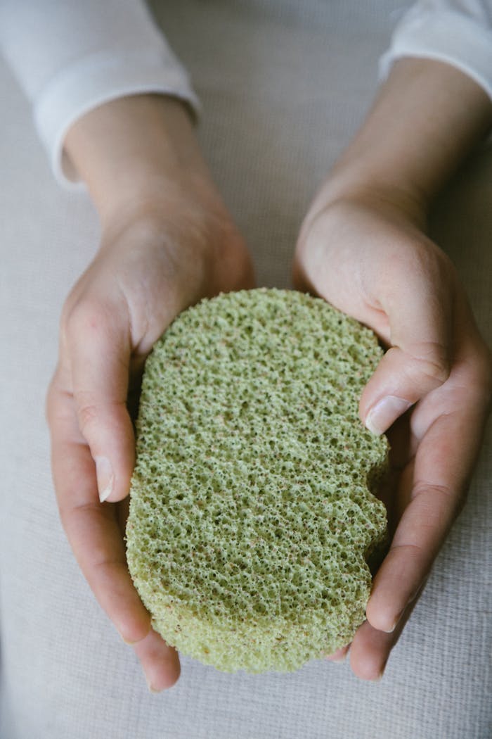 A pair of hands gently holding a green eco-friendly sponge, emphasizing sustainable self-care.